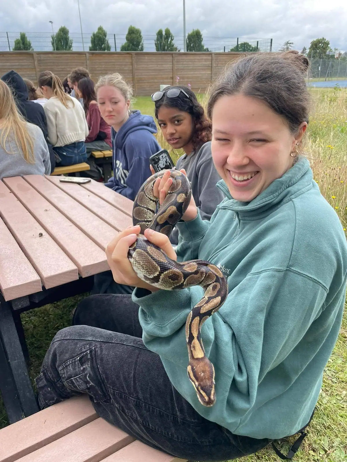 Girls in a green jumper sitting on a bench holding a live snake and laughing And Snake