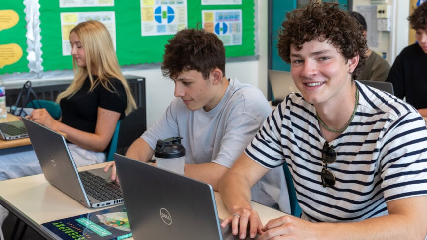 Students in a geography class working on laptops and smiling