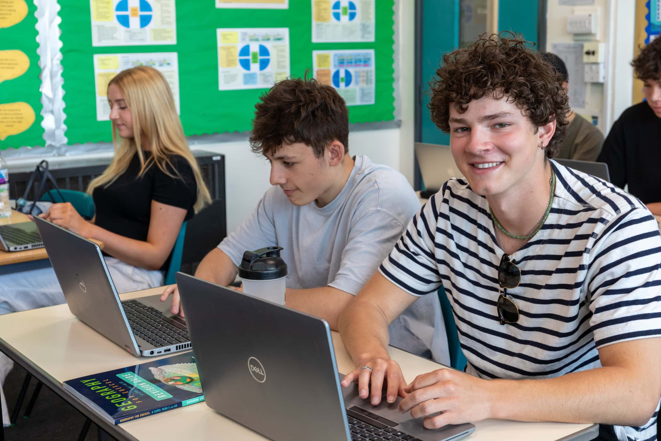 Students in a geography class working on laptops and smiling