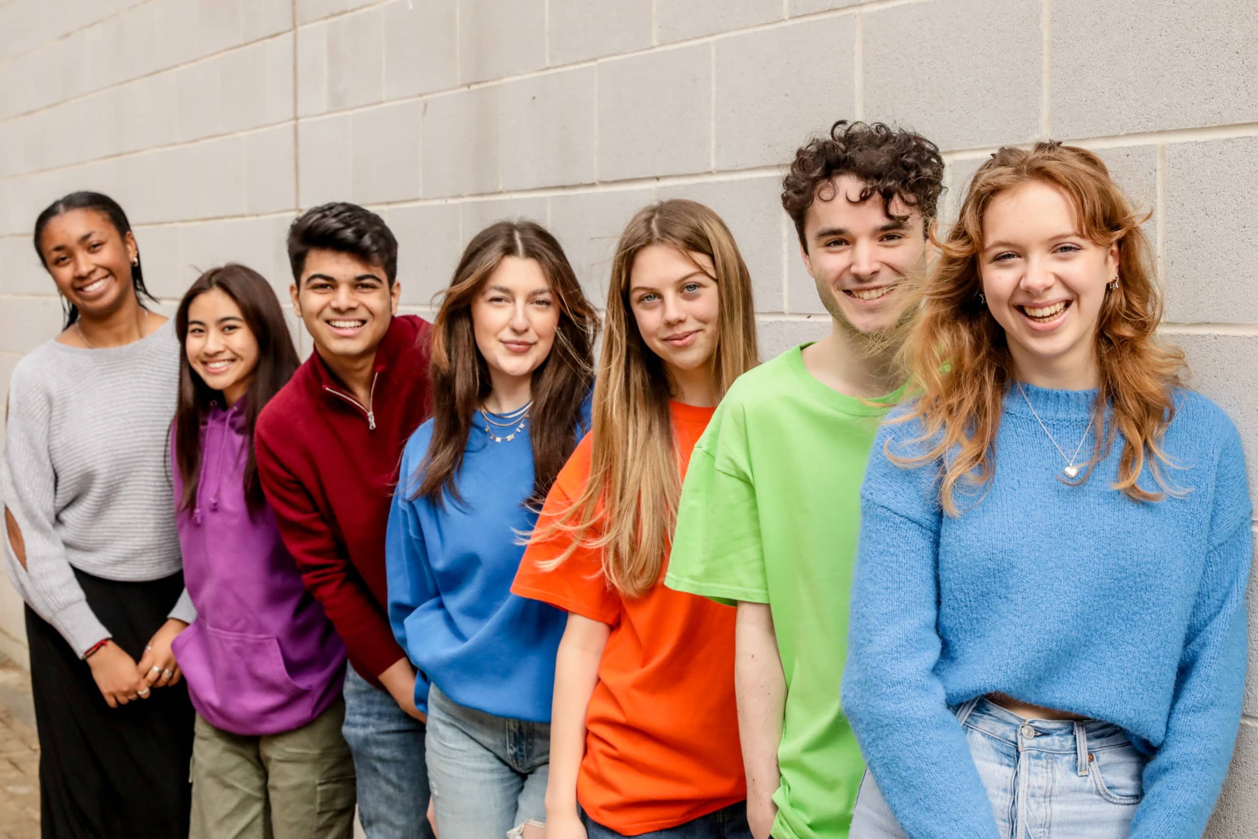 Students standing against grey wall with bright jumpers on