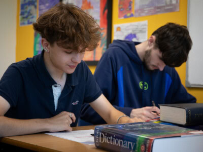Two male students writing at a desk in a classroom