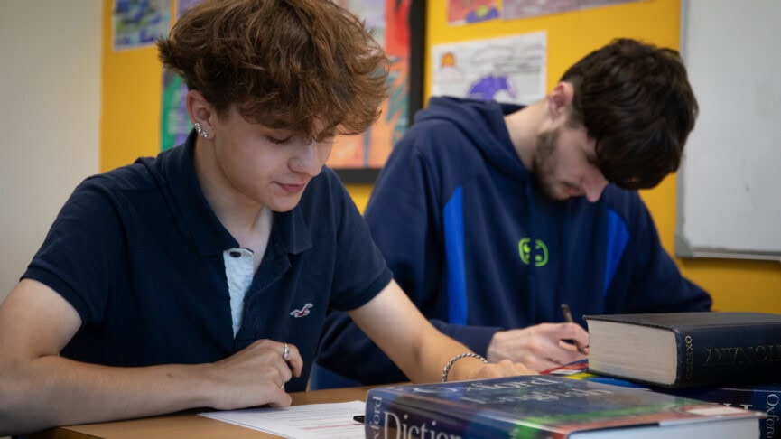 Two male students writing at a desk in a classroom