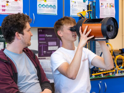 Two physics in a classroom, with one lookign into a cylinder