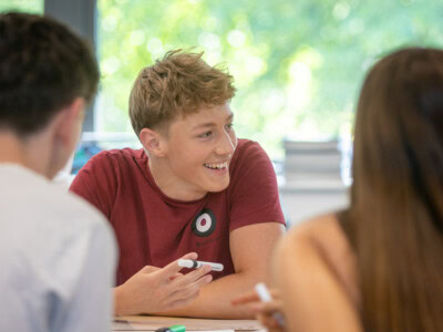 Boy sat at a table in a classroom studying and talking with friends