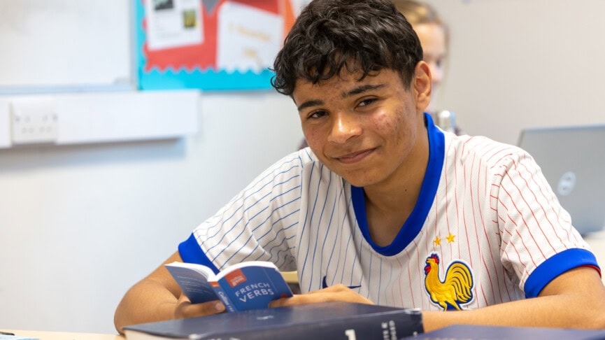 A male student sitting at a desk with a French textbook