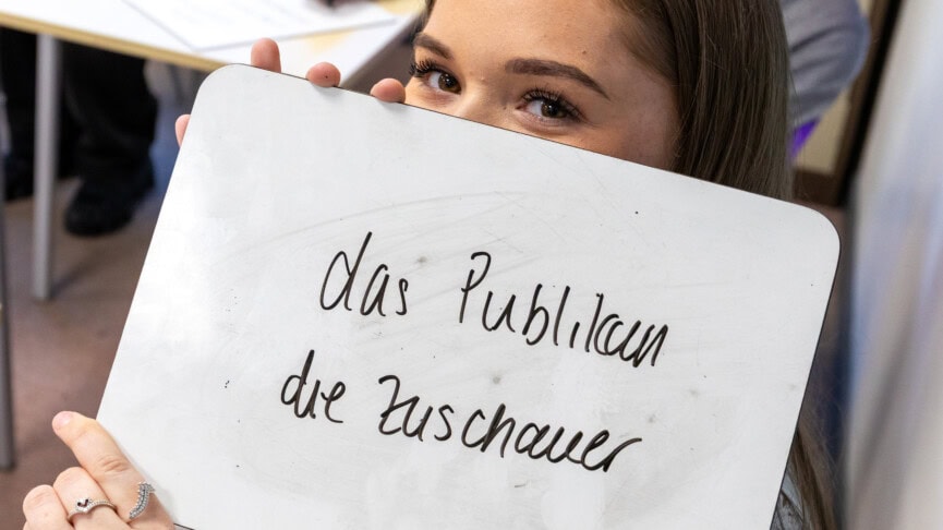 a female student hiding behind a whiteboard containing German writing