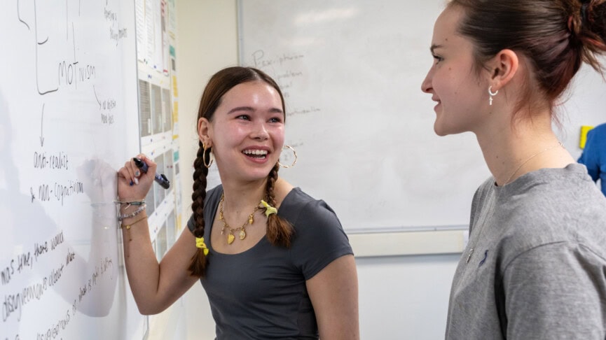 two female students working at the whiteboard in a philosophy classroom