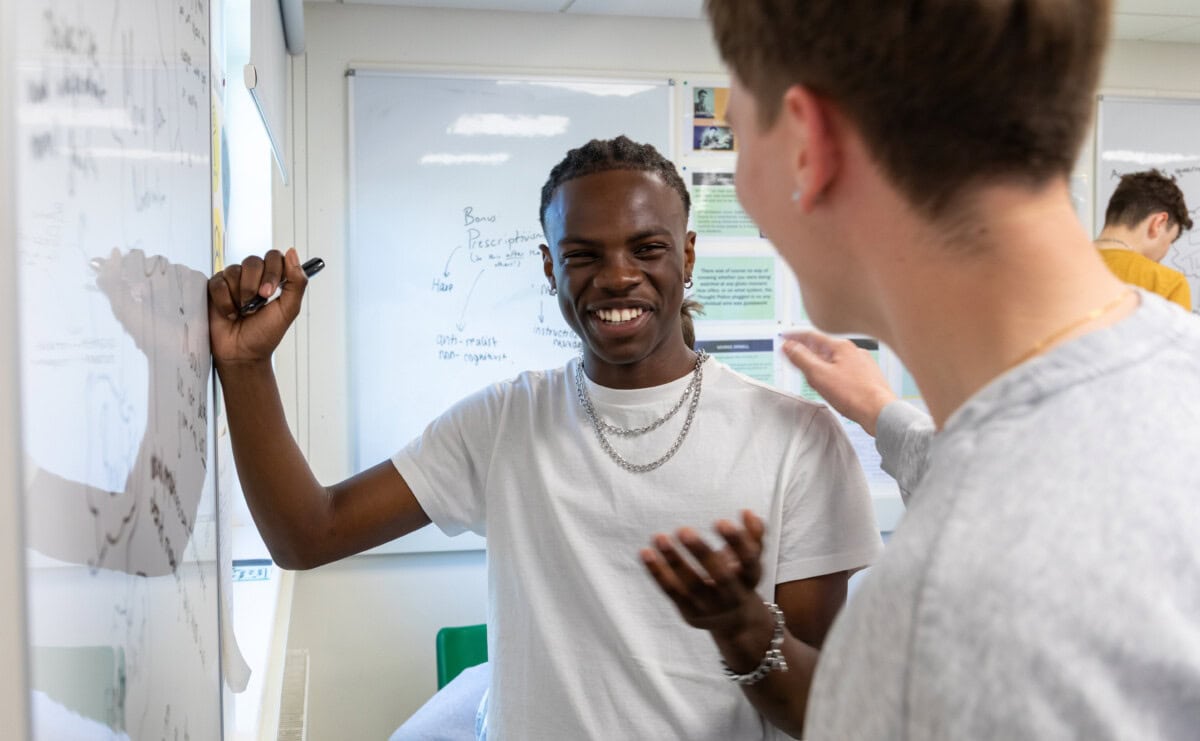 two male students having a laugh while working at the whiteboard