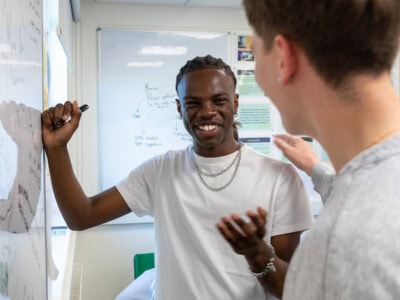 two male students having a laugh while working at the whiteboard