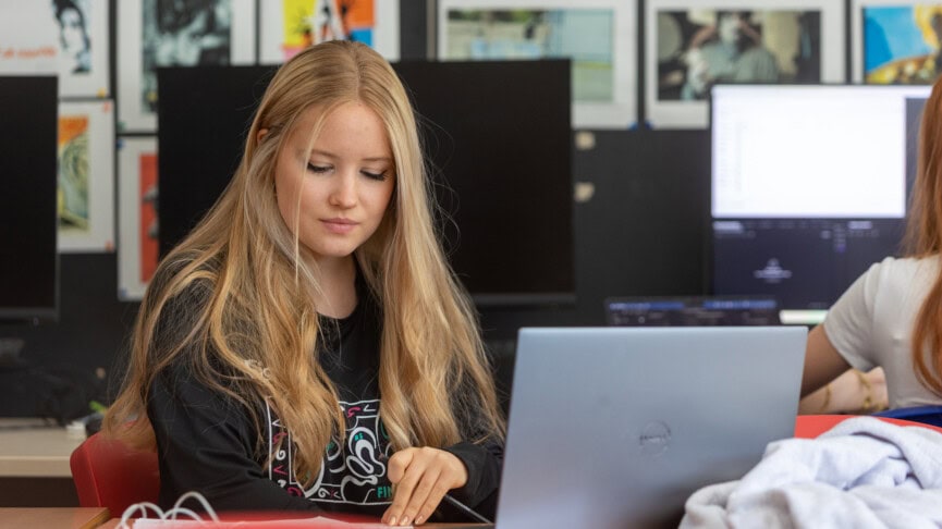 A female student with blonde hair using a laptop in a classroom