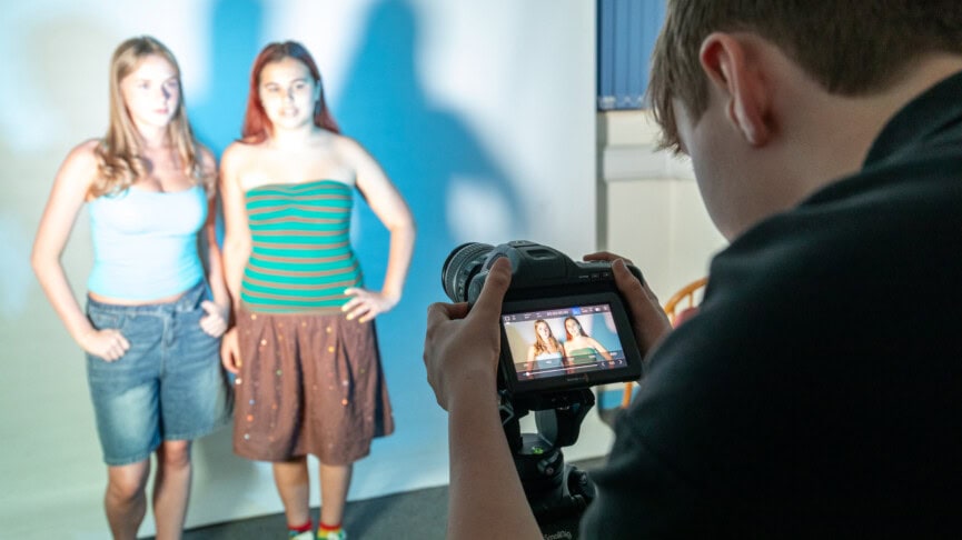 student looking at two other students through the lens of a digital camera