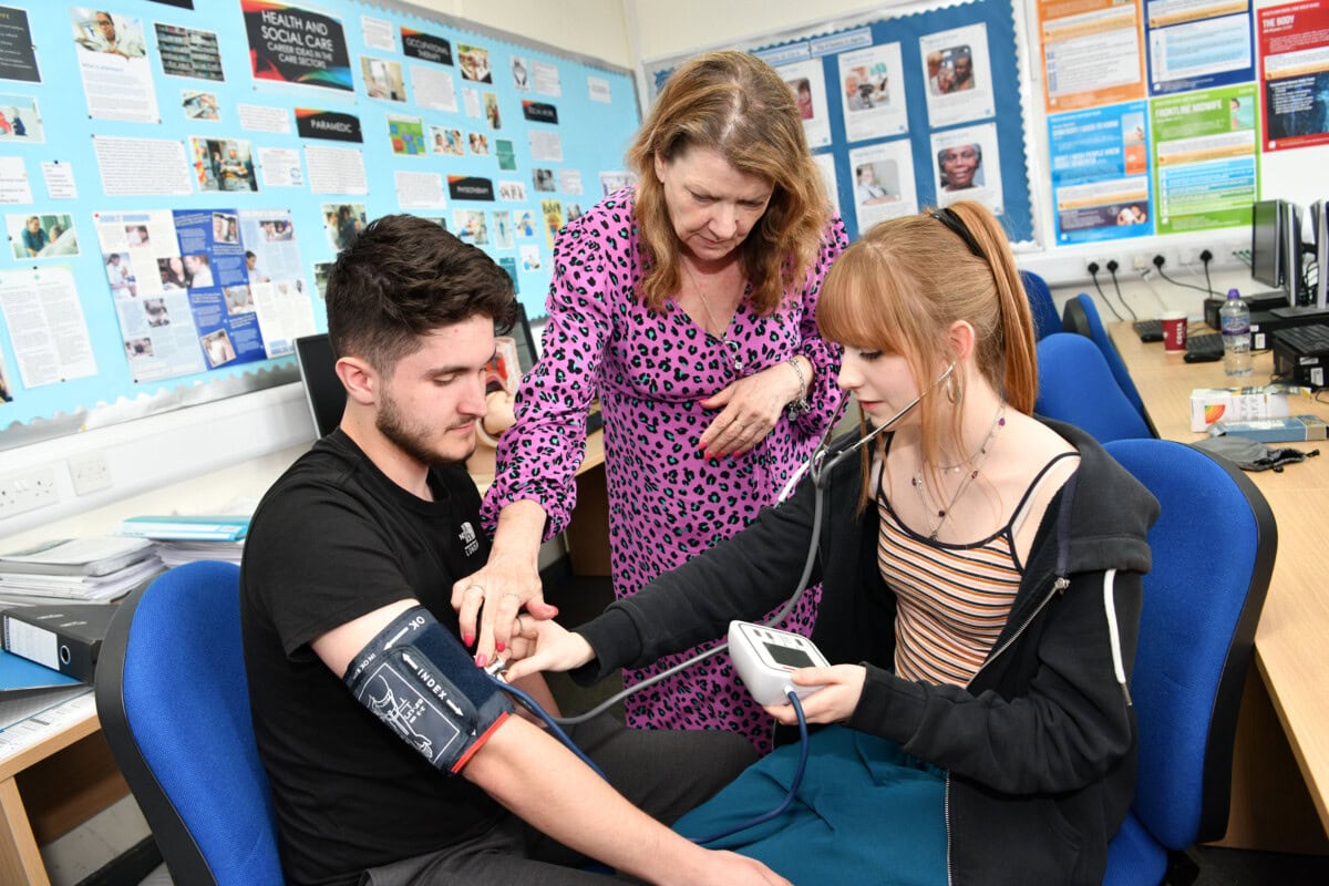 boy and girl student are shown by a teacher how to take blood pressure