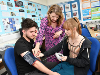 boy and girl student are shown by a teacher how to take blood pressure