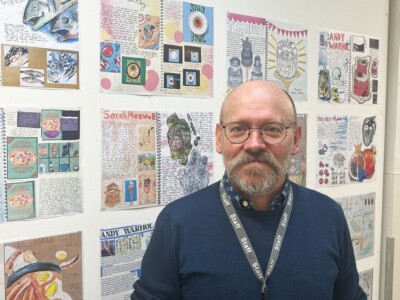 Art and design teacher Nick Saunders standing in front of a wall of graphic art created by students