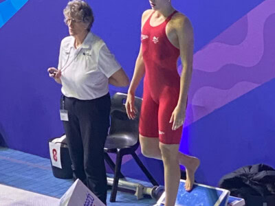 Swimmer in a red costume at the podium about to dive into pool