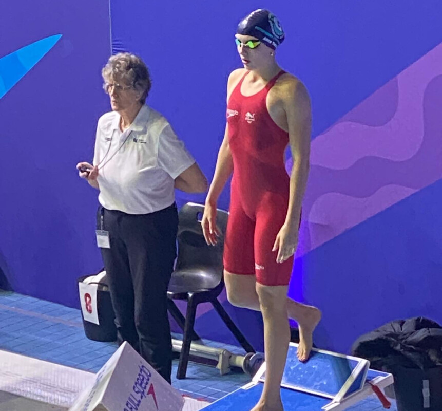 Swimmer in a red costume at the podium about to dive into pool