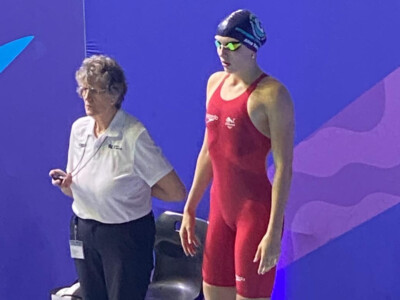 Swimmer in a red costume at the podium about to dive into pool