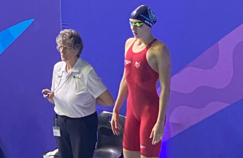 Swimmer in a red costume at the podium about to dive into pool