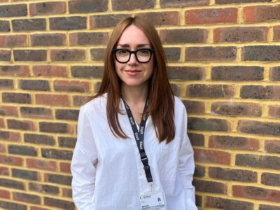 woman wearing a white shirt stands infront of a brick wall