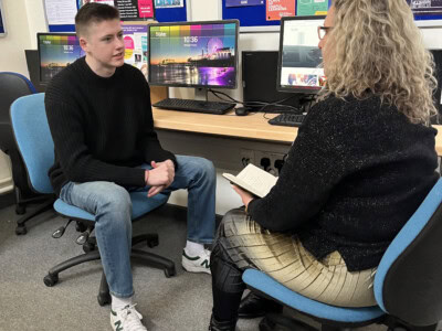 A student and teacher sitting at a computer and chatting