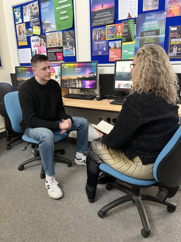 A student and teacher sitting at a computer and chatting
