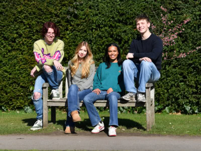 four students sit on a college bench, two girls in the middle and two boys sitting on either side.