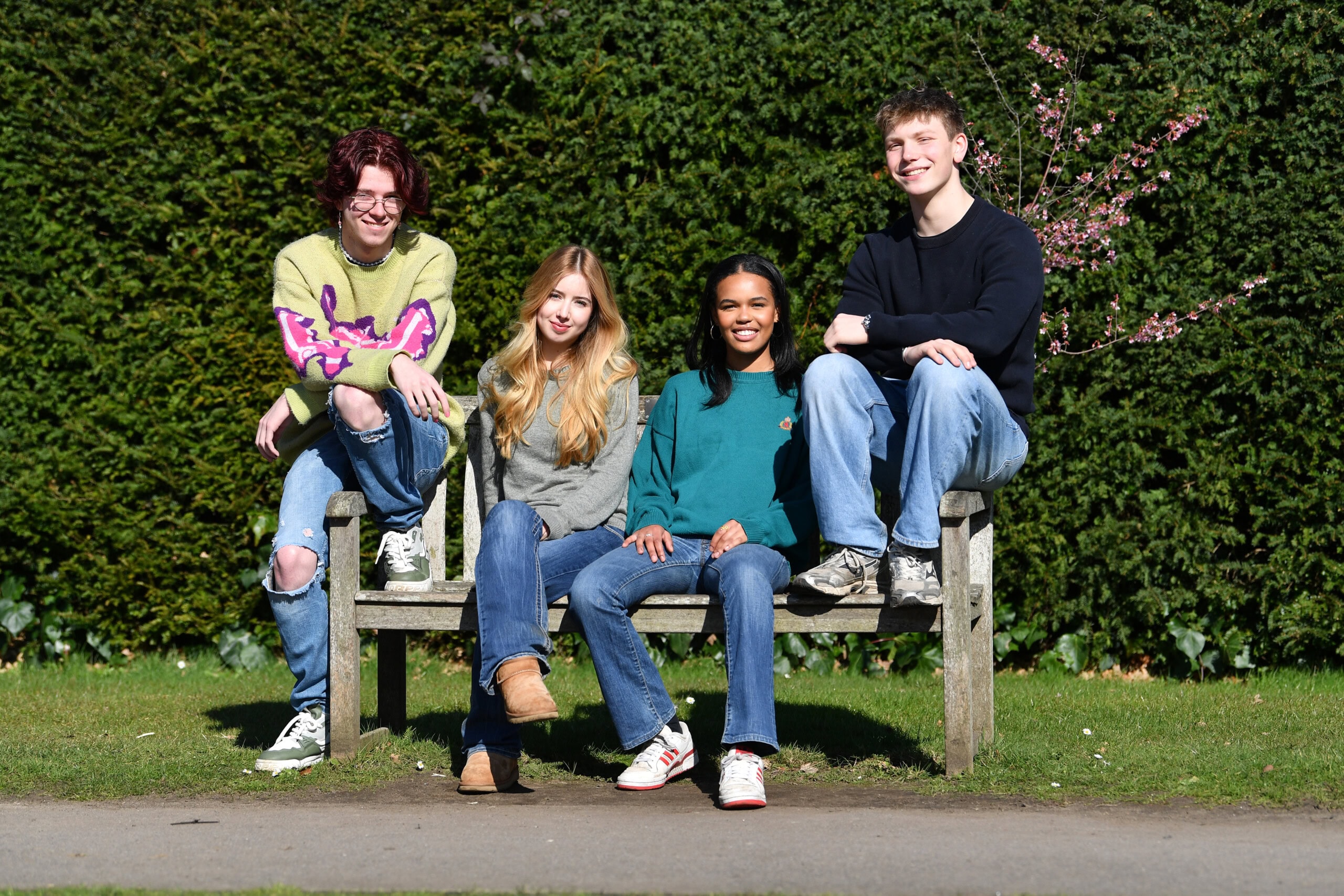 four students sit on a college bench, two girls in the middle and two boys sitting on either side.
