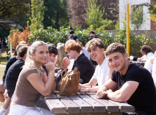 a group of students sitting at a table out in the sunshine