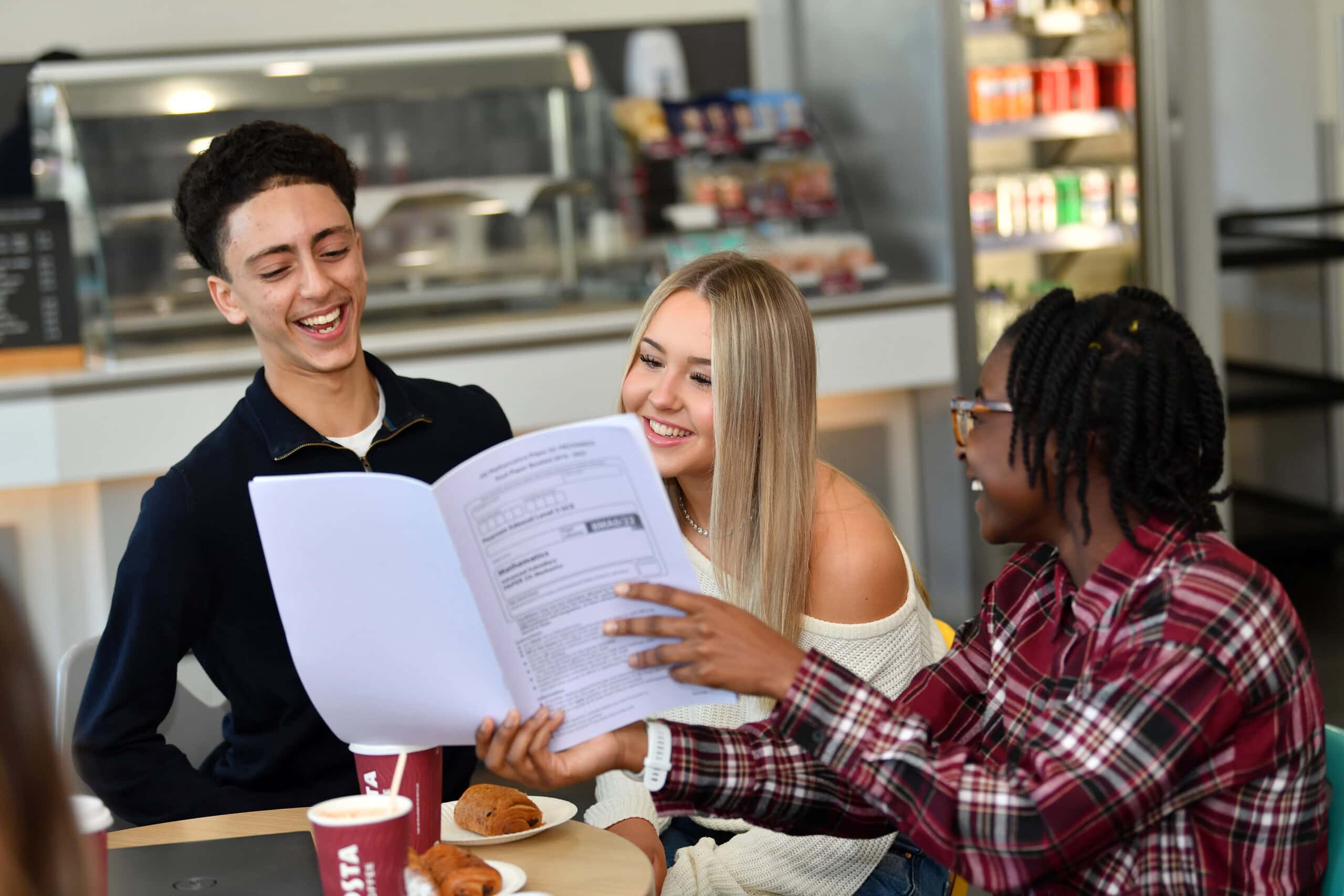 three students in the cafe having a giggle over a document