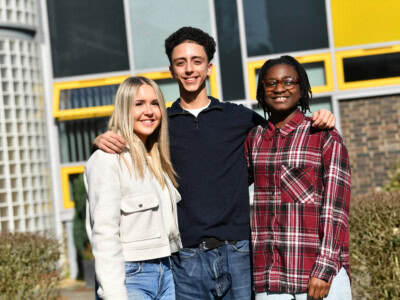 Three students standing with their arms around each other at the front of the college