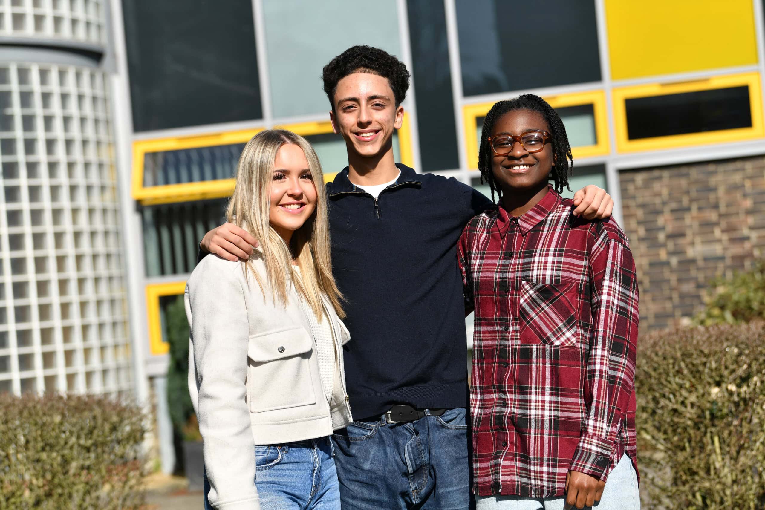 Three students standing with their arms around each other at the front of the college