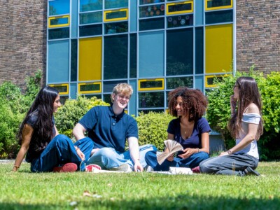 Four students sitting outside the College in the sun