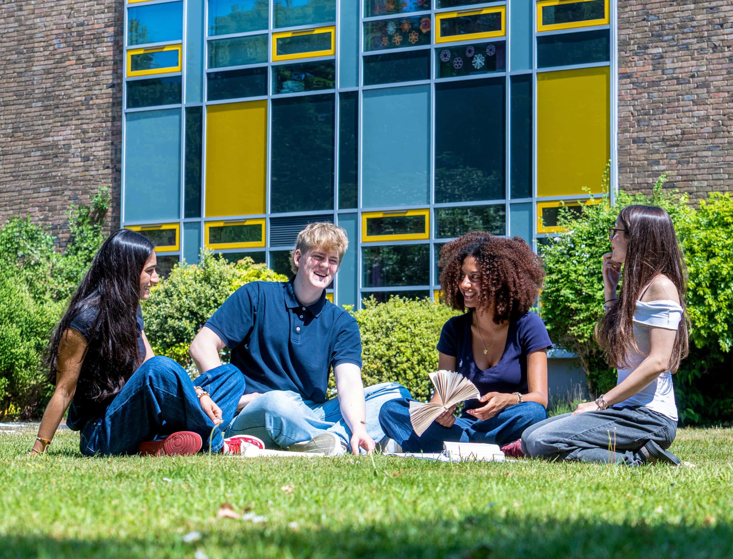Four students sitting outside the College in the sun