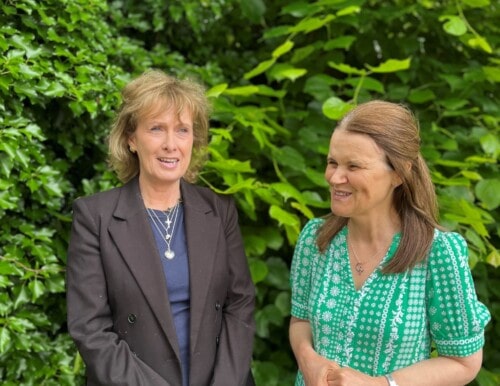Two staff members Jo Canessa and Sue Ockleford standing in front of a bush laughing