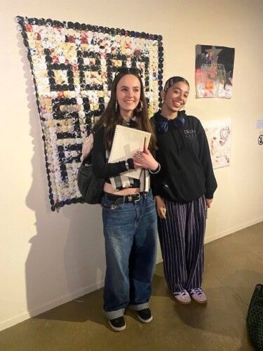 Fashion students holding a sketchbook in front of an exhibition