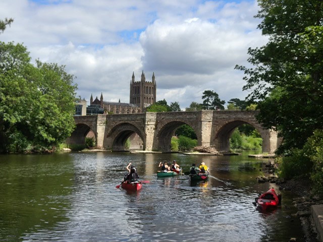 Student Canoeing In Front Of A Bridge