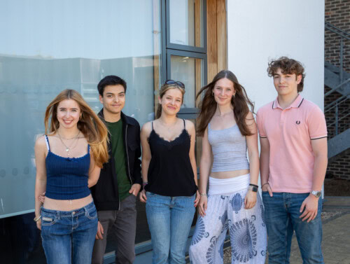 Three girls and two boy students stand by the dance studio