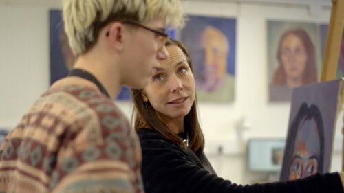 ARt teacher works with a male student at his easel