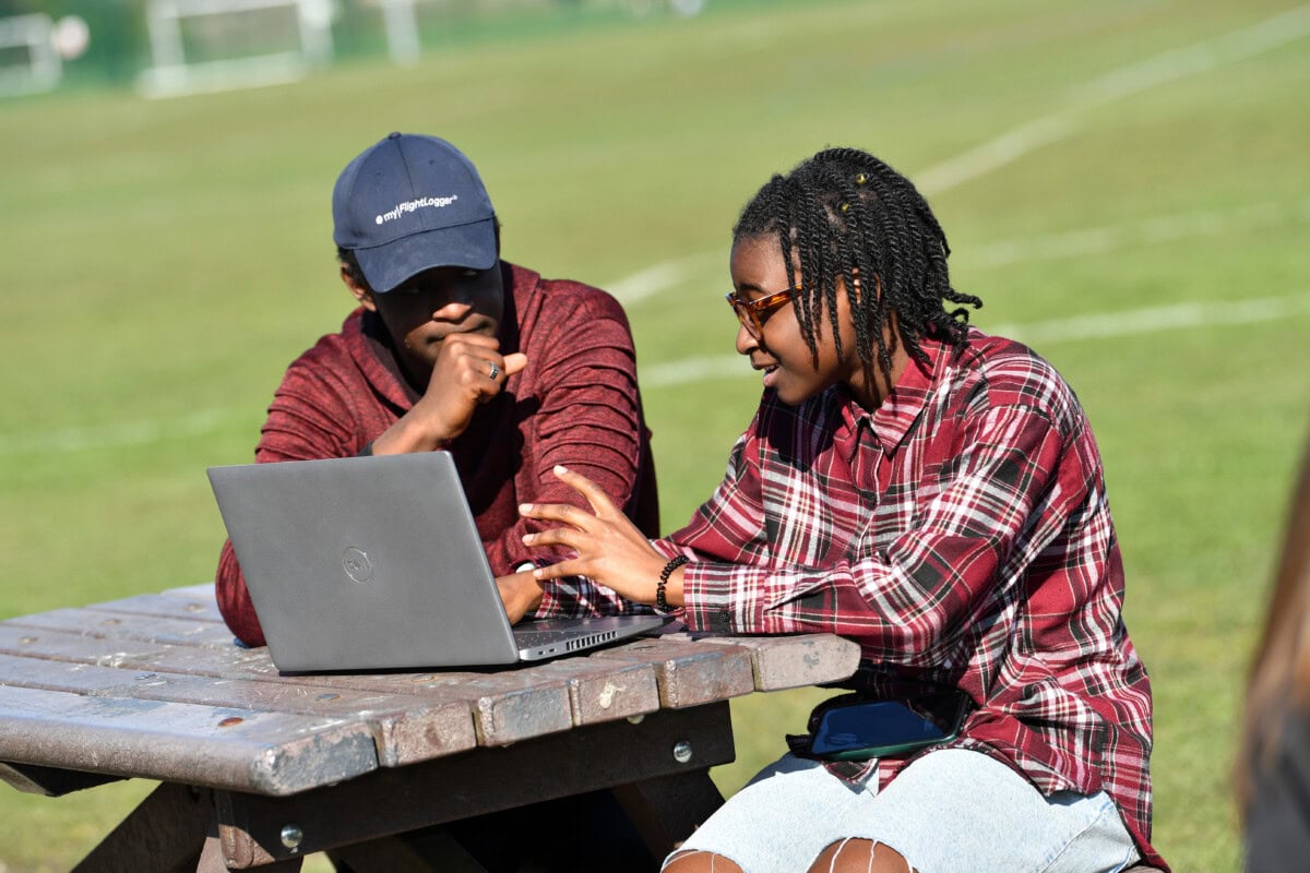 two students sitting outside and looking at a laptop