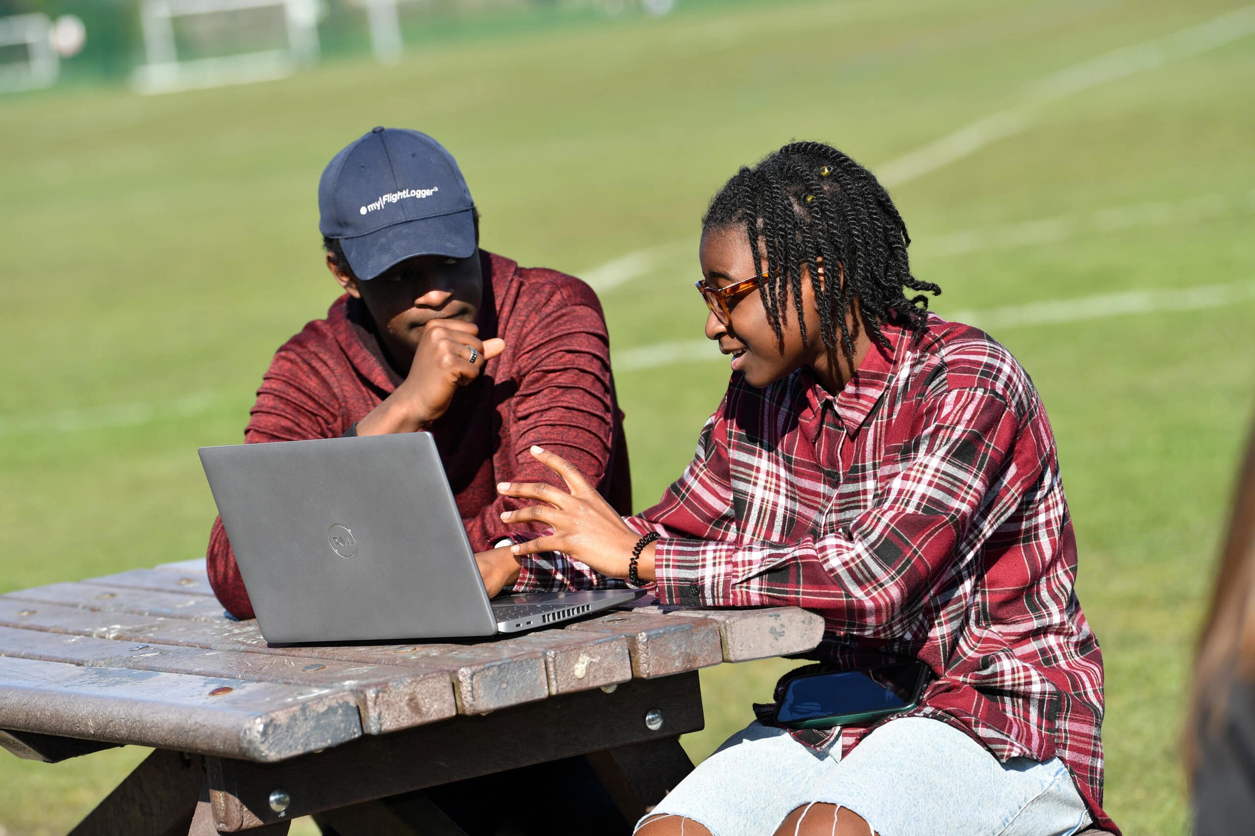 two students sitting outside and looking at a laptop