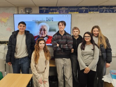 students standing in front of a screen featuring Baroness Harris Of Richmond