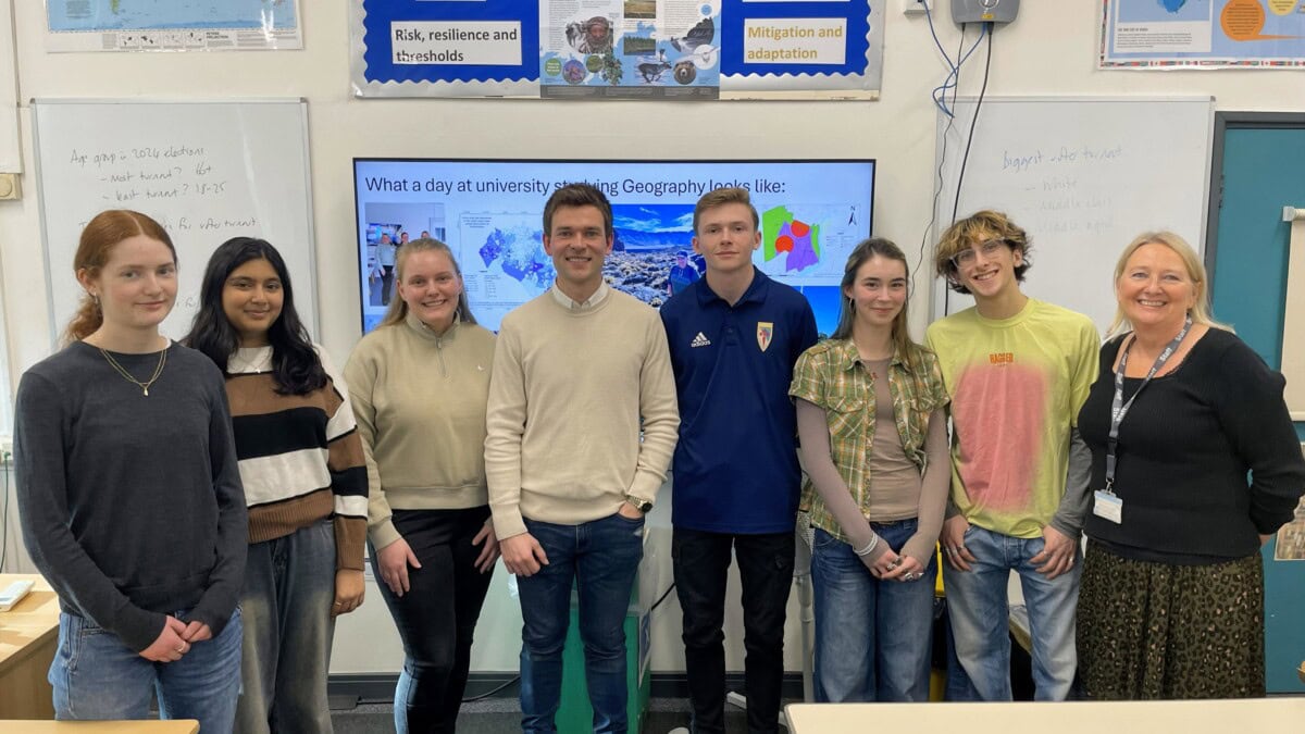 A group of geography students, teachers and guest speakers stand in a line in a classroom