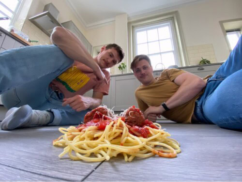 James Goodchild And Comedy Partner In Fron Of A Pile Of Spaghetti