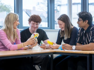 Four students sit at a desk in a psychology lesson discussing a model of a brain