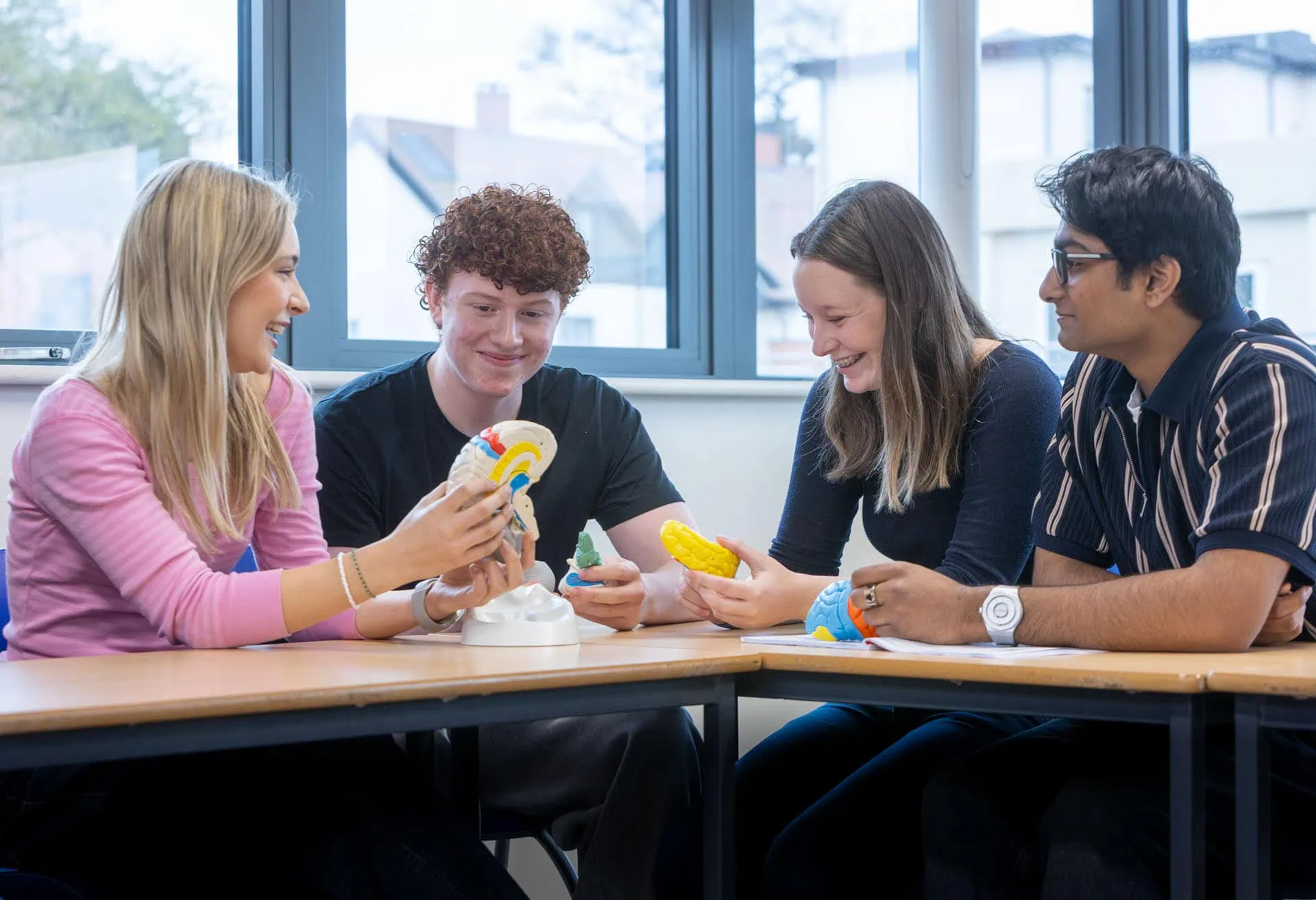 Four students sit at a desk in a psychology lesson discussing a model of a brain