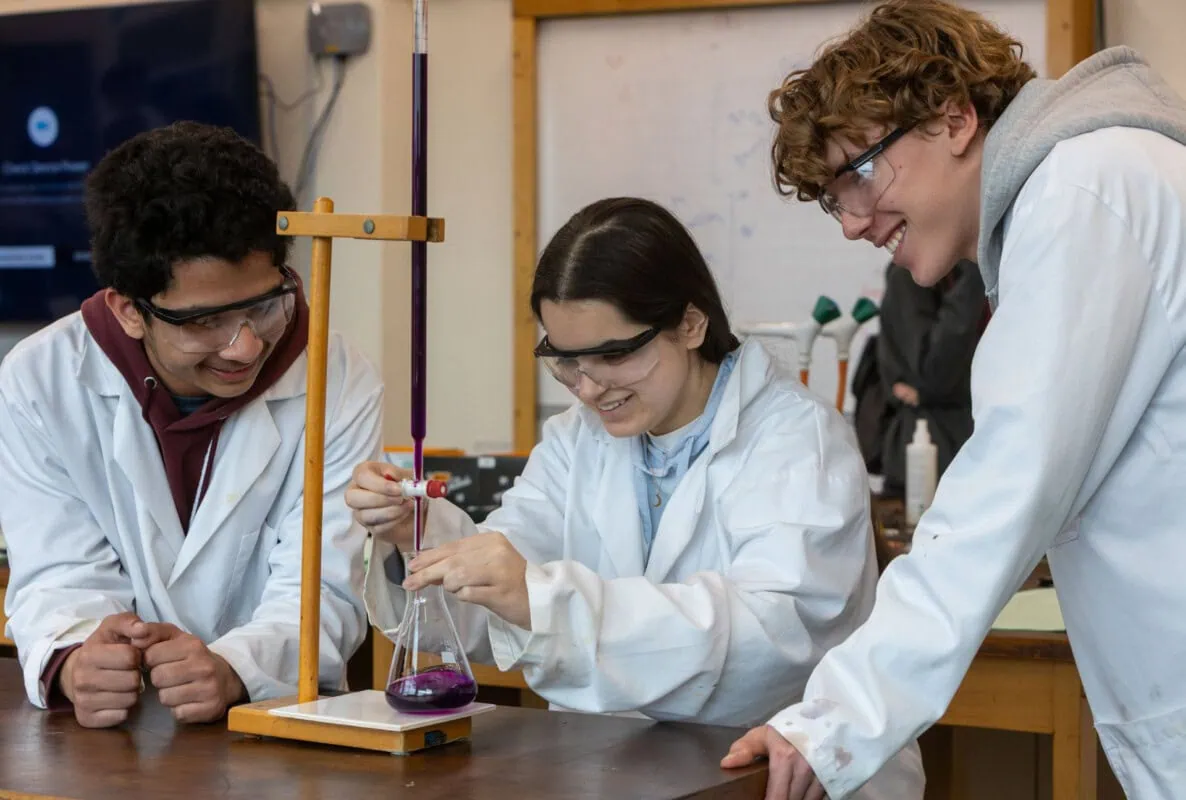 3students in white lab coats conduct an experiment