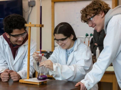 3students in white lab coats conduct an experiment