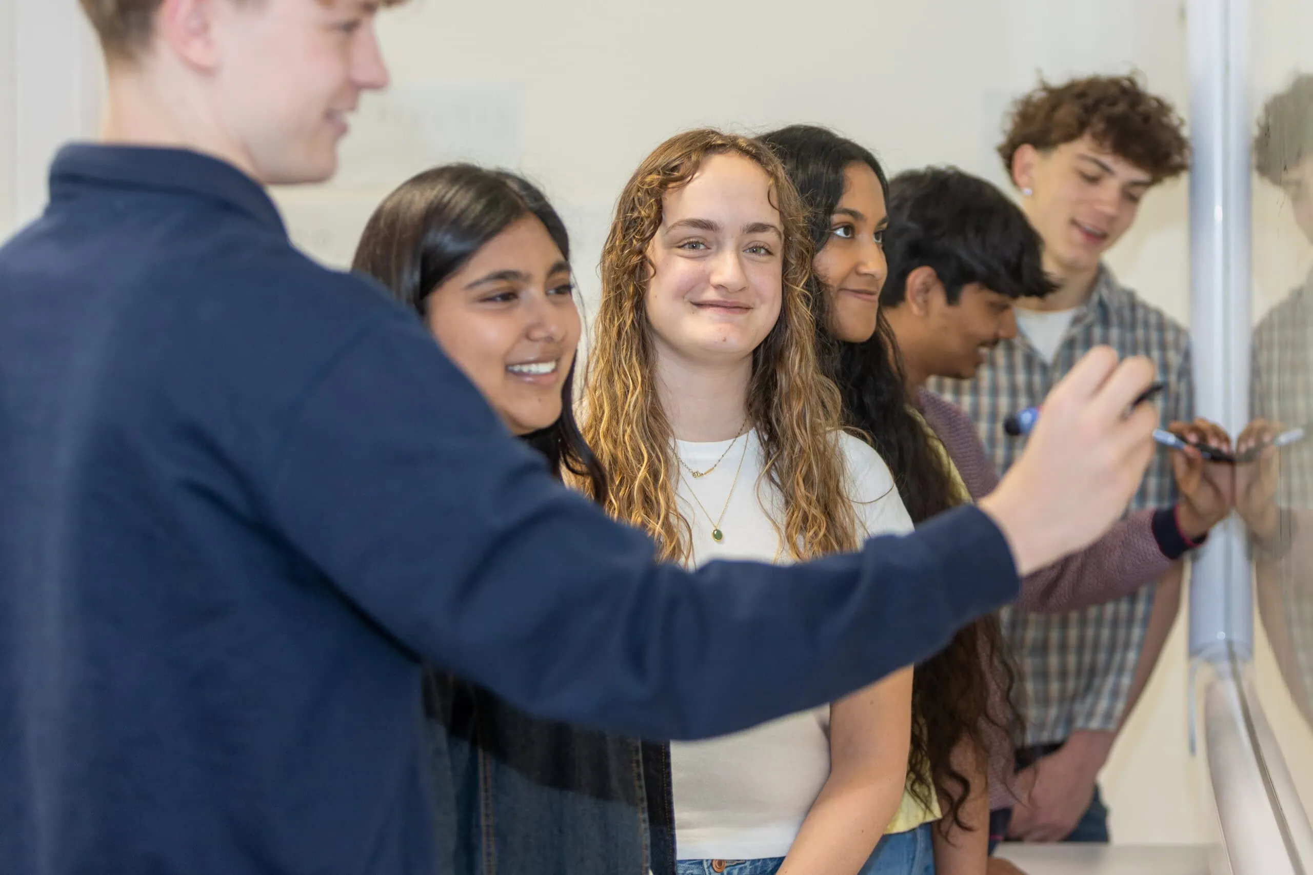 students working at a white board with one student looking at camera