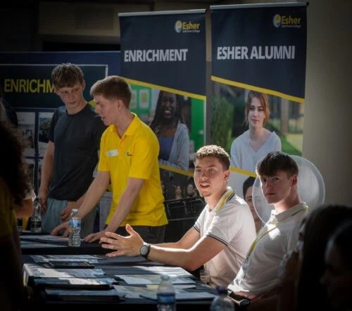 two young men sit at an alumni stand at Esher open evening