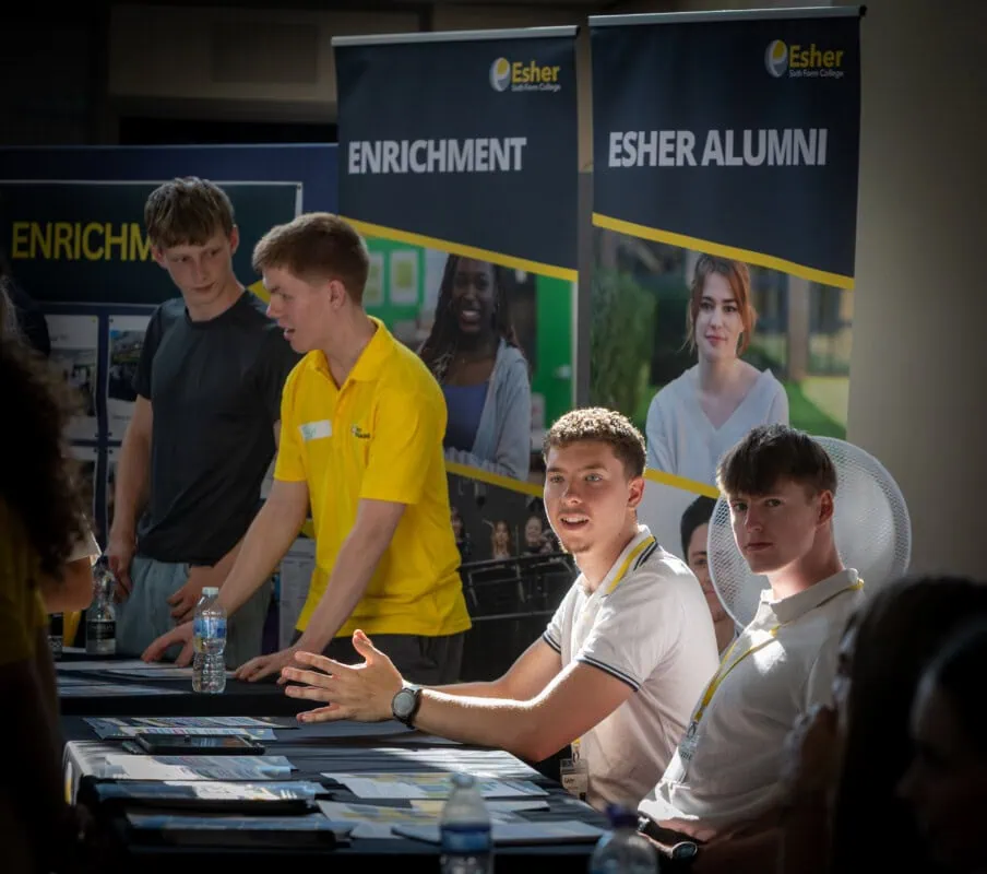 two young men sit at an alumni stand at Esher open evening